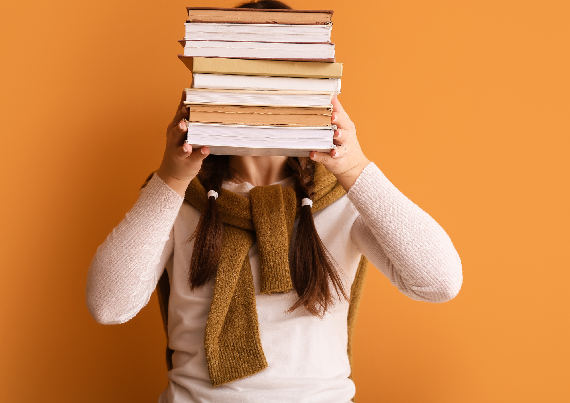 Eine Frau hält einen Bücherstapel vor ihr Gesicht.