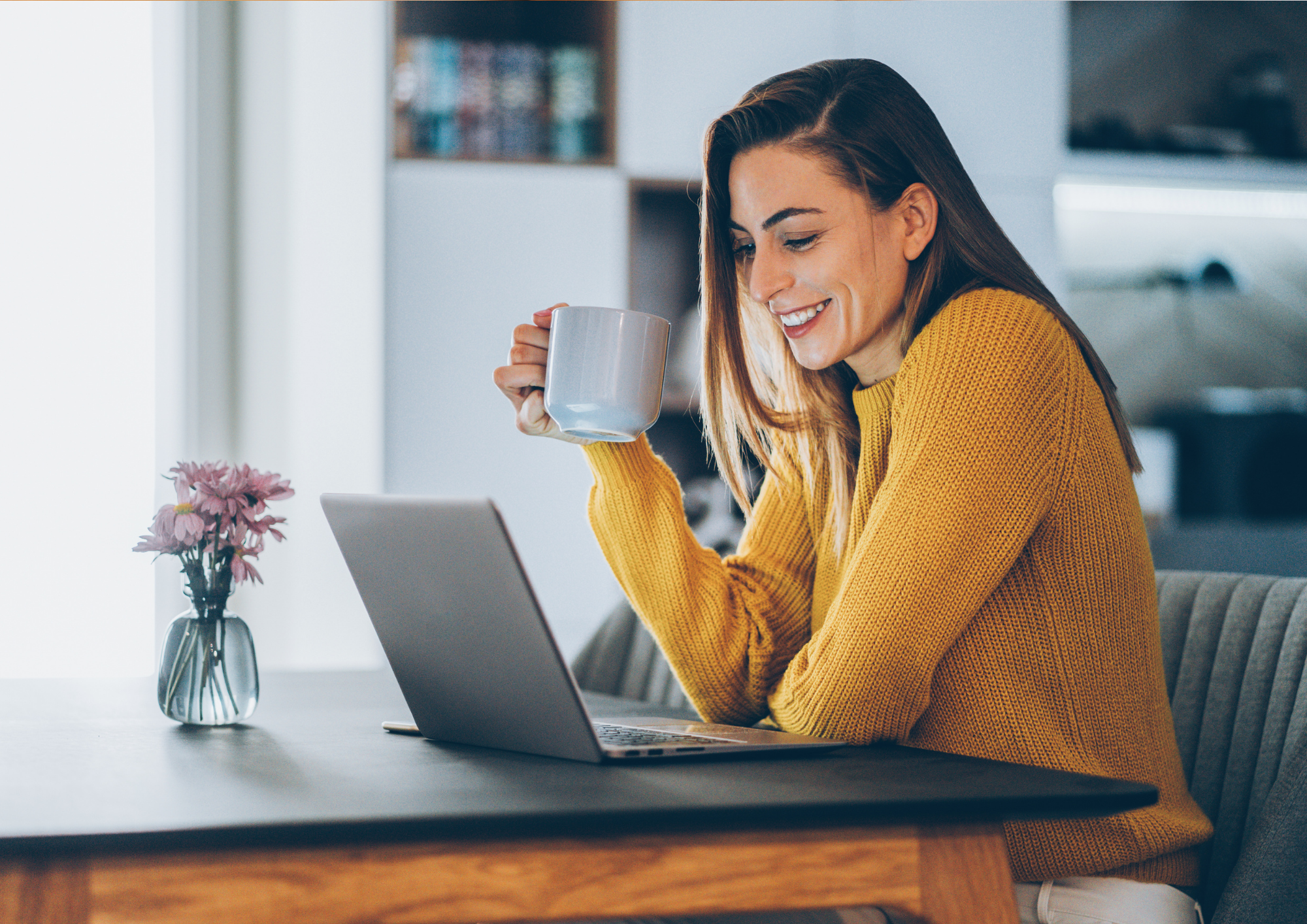 Eine Frau sitzt mit Laptop und Tasse an einem Tisch.